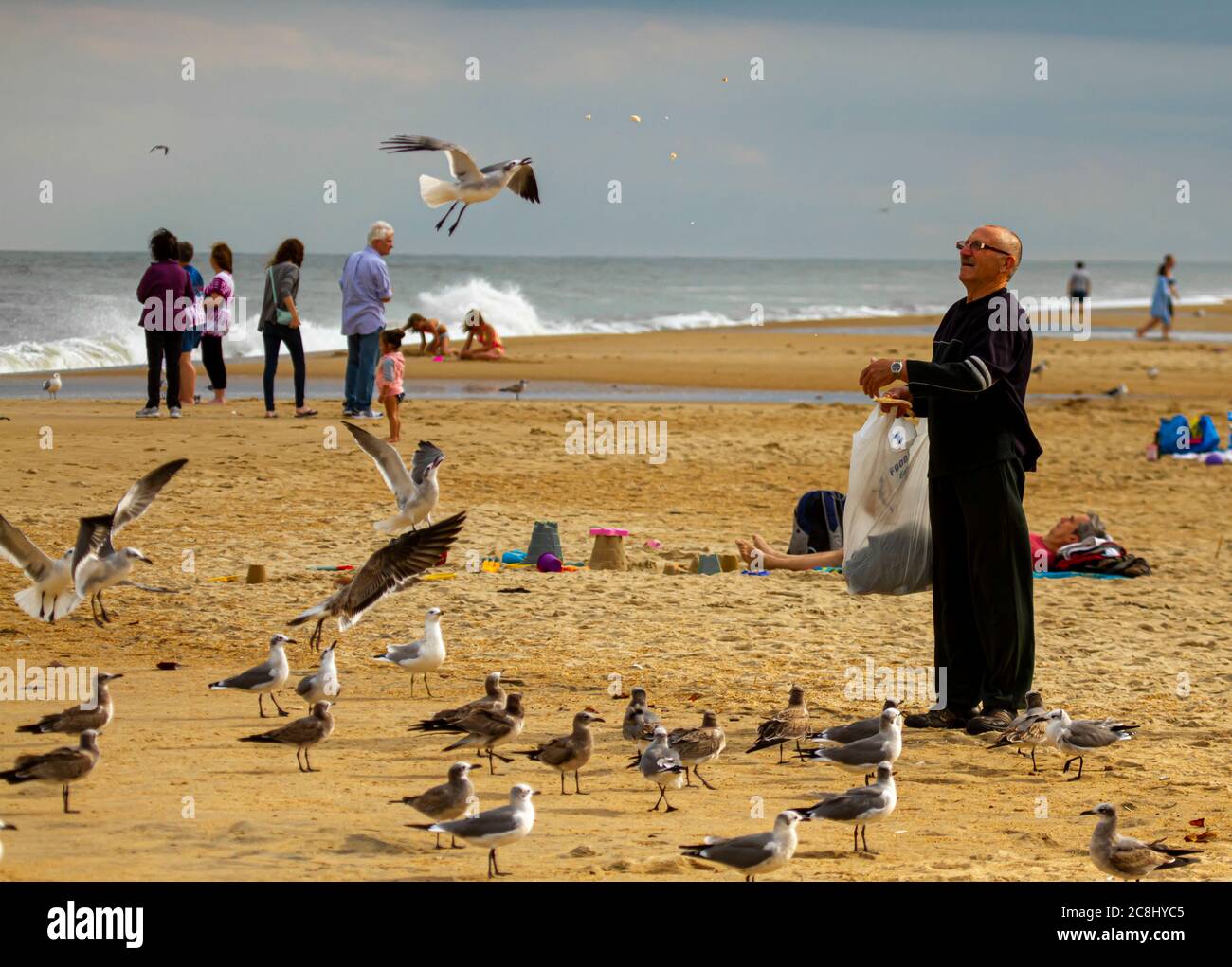 Delaware, USA 10/04/2014: Ein alter Mann in schwarzen Kleidern wirft Seemöwen am Strand mit Seemöbeln. Vögel versammelten sich um ihn herum und einige fliegen Stockfoto