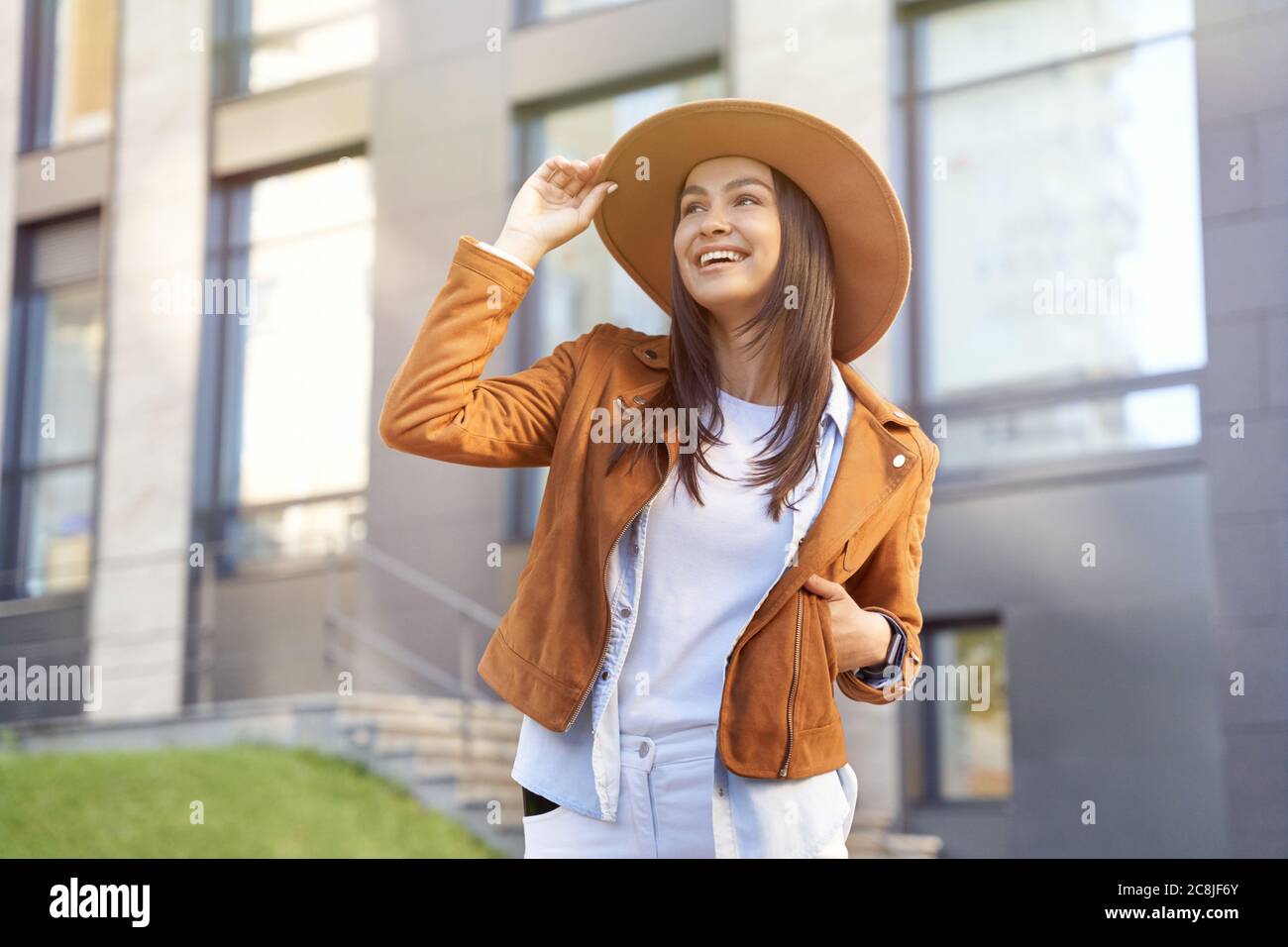 Stadtspaziergang. Porträt einer glücklichen schönen Frau, die ihren Hut berührt, während sie auf der Straße der Stadt geht, lächelt und sonniges Wetter genießt. Menschen Konzept, urbane Lebensweise Stockfoto