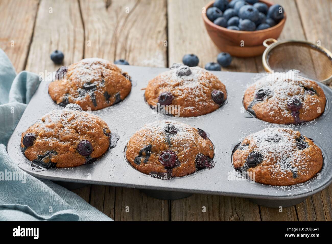 Blaubeer Muffin im Tablett, Seitenansicht. Cupcakes mit Beeren in Backform auf alter Leinenserviette, rustikaler Holztisch, Frühstück mit Kuchen Stockfoto