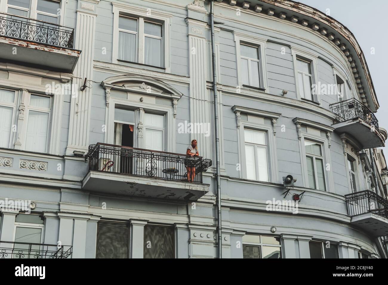 Ukraine, Odessa - 23. August 2019: Mädchen auf dem Balkon eines neoklassizistischen Gebäudes bei Sonnenuntergang. Stockfoto