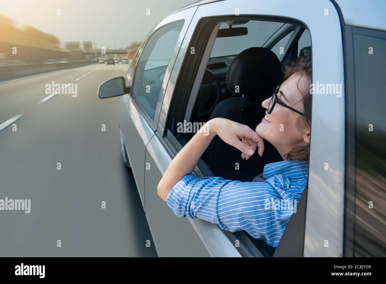 Beifahrerin sitzt auf dem Rücksitz und schaut aus dem Fenster, wenn ihr selbstfahrendes Auto auf der Autobahn fährt. Stockfoto