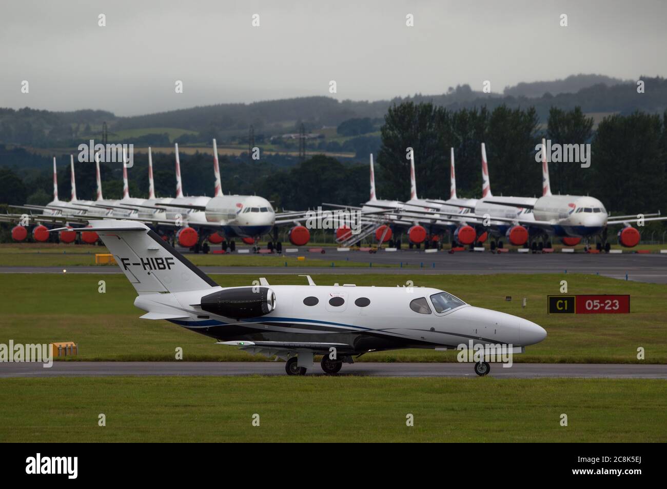 Glasgow, Schottland, Großbritannien. 23. Juli 2020. Im Bild: Ein Cessna 510 Citation Mustang Privatjet (reg F-HIBF) vor dem Hintergrund eines geerdeten Airbus A319/A320/A321 von British Airways (BA) sitzt auf der zweiten Landebahn des Flughafens Glasgow und wartet auf sein Schicksal, verkauft oder gelagert zu werden. Seit März sitzen diese Flugzeuge auf dem Asphalt der Flughäfen untätig, was der weltweiten Krise des Coronavirus (COVID19) zusteht. Quelle: Colin Fisher/Alamy Live News. Stockfoto