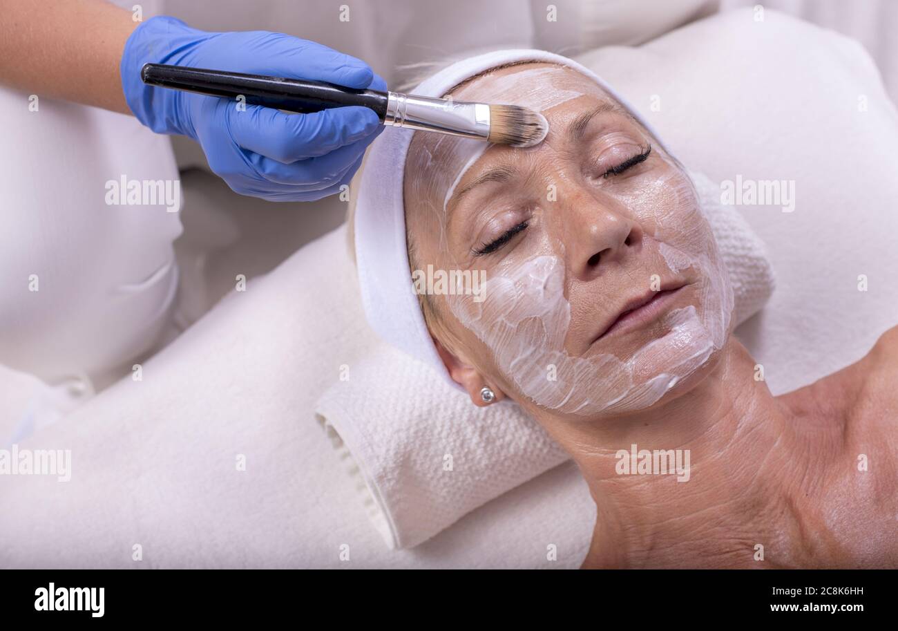 Person mit blauen Gummihandschuhen, die eine weiße crème über verbreiten Das Gesicht einer Frau Stockfoto