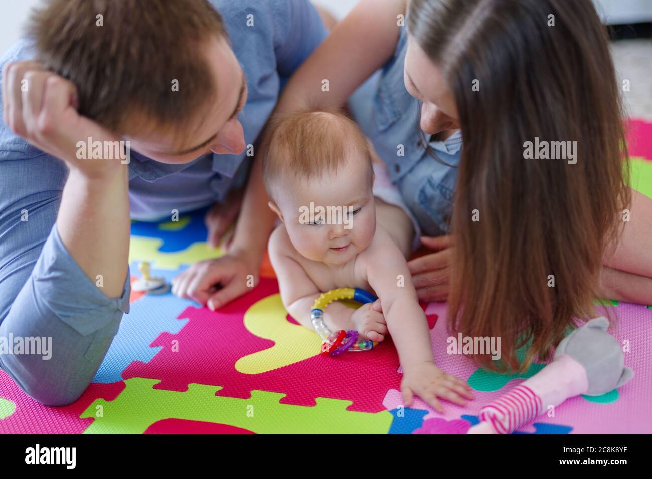 Mutter und Vater zusammen mit ihrer Tochter auf bunten Puzzle-Spielmatte Stockfoto