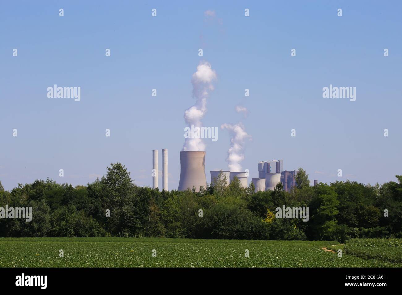 Grevenbroich, Deutschland - 9. Juli. 2020: Blick über Ackerfeld und Wald auf Braunkohlebergbau RWE Kraftwerk Frimmersdorf Stockfoto