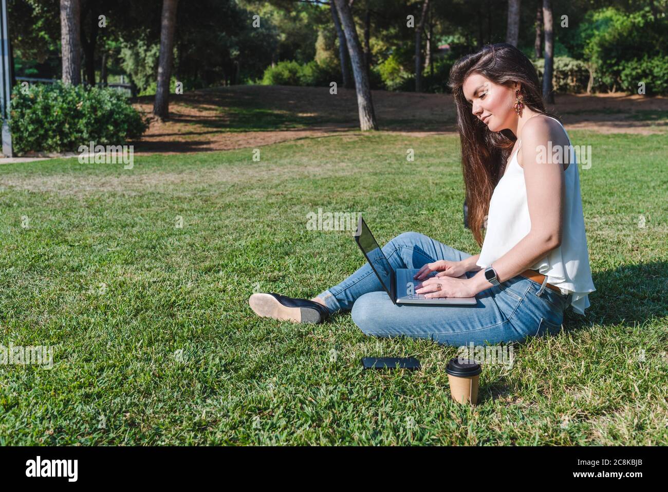 Schöne junge kaukasische Frau, die auf dem Gras eines Parks sitzt und mit einem Laptop arbeitet Stockfoto
