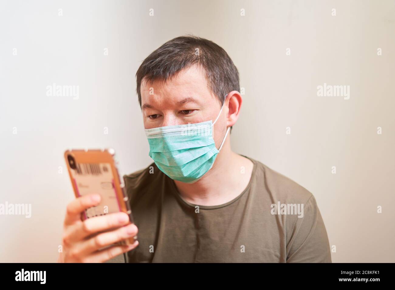 Ein Mann in einer medizinischen Maske schaut auf das Telefon, eine Online-Bestellung zur Selbstuntersuchung, Quarantäne, zu Hause bleiben, online Stockfoto