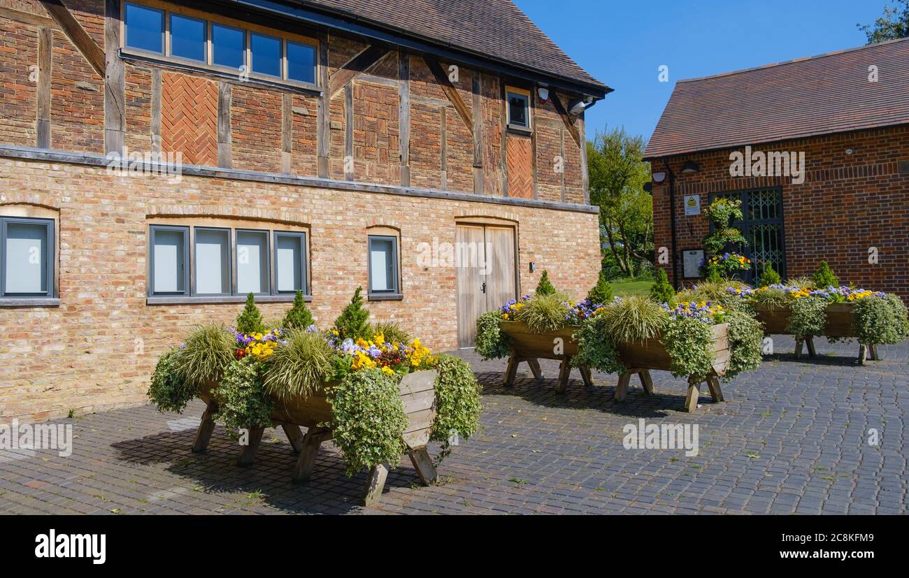 The Stables, Fachwerkgebäude aus dem 17. Jahrhundert, mit Holzpflanzen, lila & gelben Blumen & Laub, Eastcote House Gardens, Eastcote, London. Stockfoto