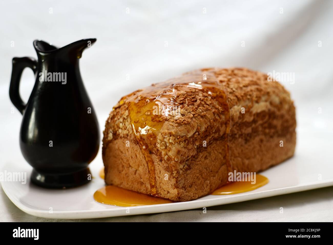 Süßer Honig im schwarzen Glas und Weizenbrot in weißem Teller. Stockfoto