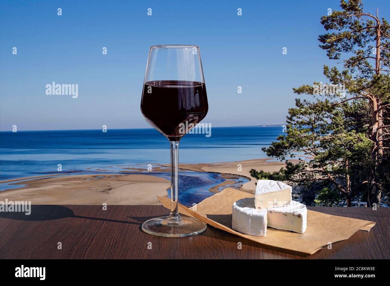 Ein Glas Rotwein mit Brie-Käse mit Blick auf die Weiße Düne und den Baltischen See im Frühjahr, Lettland. Strand mit weißem Sand und blauem Meer. Stockfoto