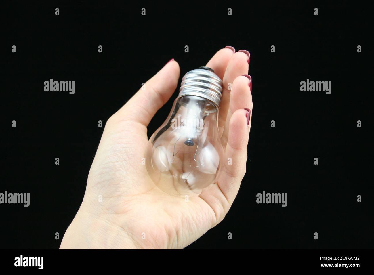 Die Hand der Frau hält eine klare Glühbirne mit einem schwarzen Hintergrund. Stockfoto