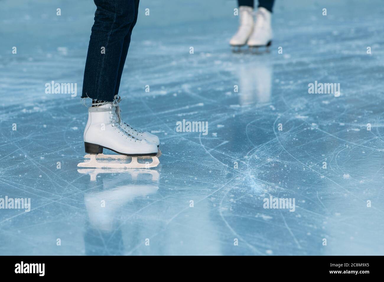 Nahaufnahme der Beine des Eislaufes auf der Eisbahn im Freien. Frau steht in weißen Schlittschuhe. Wochenend-Aktivitäten im Freien bei kaltem Wetter. Stockfoto