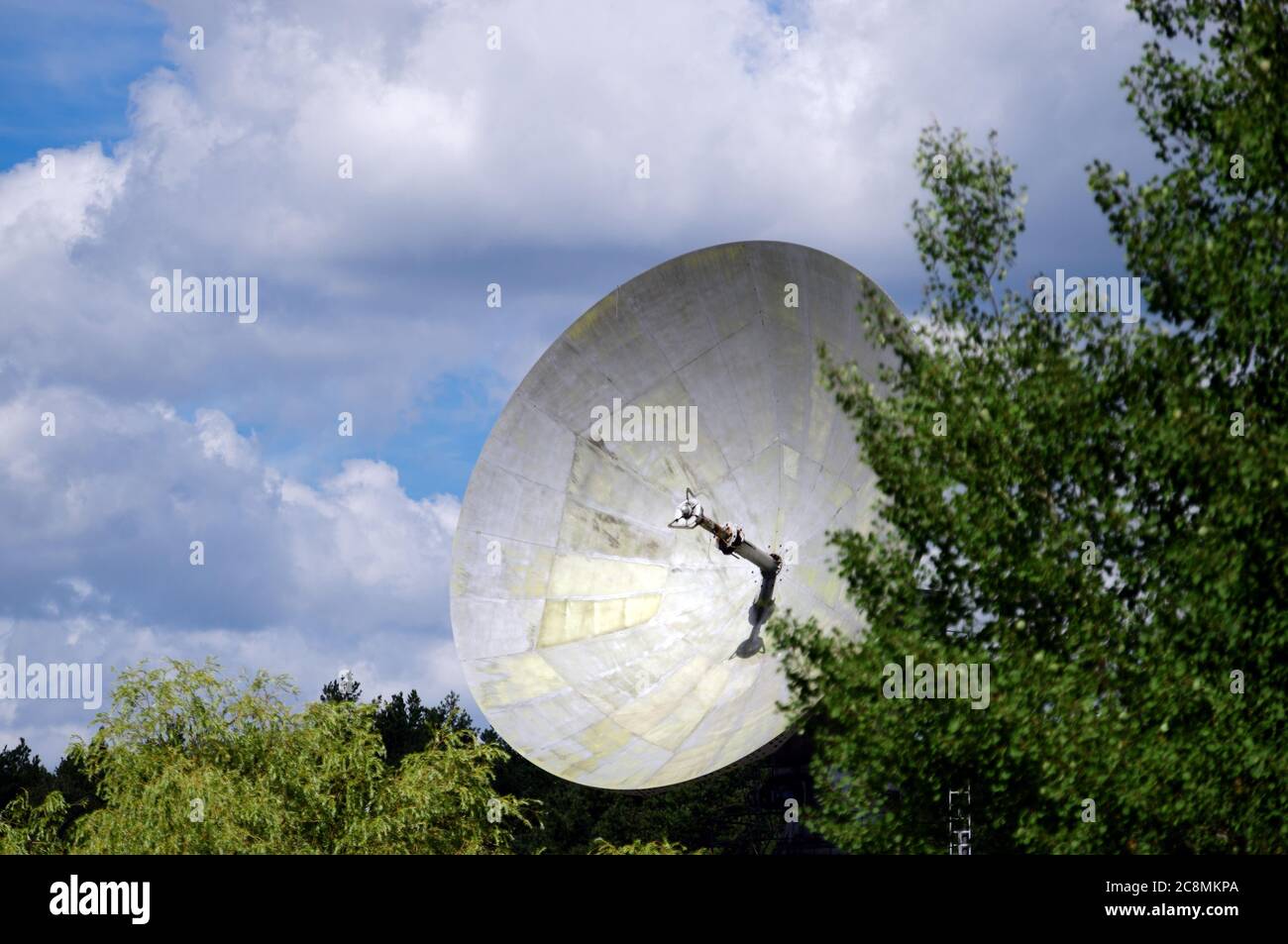 22. Juli 2020, Brandenburg, Bad Saarow/OT Neu-Golm: Zwischen den Bäumen ist die 12 Meter lange Parabolantenne der ehemaligen Satellitenbodenstation Intersputnik zu sehen. Die Erdstation war in DDR-Zeiten die einzige Station zur Übertragung kommerzieller Kommunikationsdaten und wurde von 1875 bis 1996 betrieben. Signale von Telefon, Fernsehen und Radio wurden empfangen und übertragen. Unter anderem gab es zu Beginn des regulären Telefonbetriebs am 01.04.1976 zwei öffentliche Telefonkanäle nach Havanna. Nach der Schließung wurde die gesamte Technik demontiert. Seit 2002 ist das Gebäude h Stockfoto