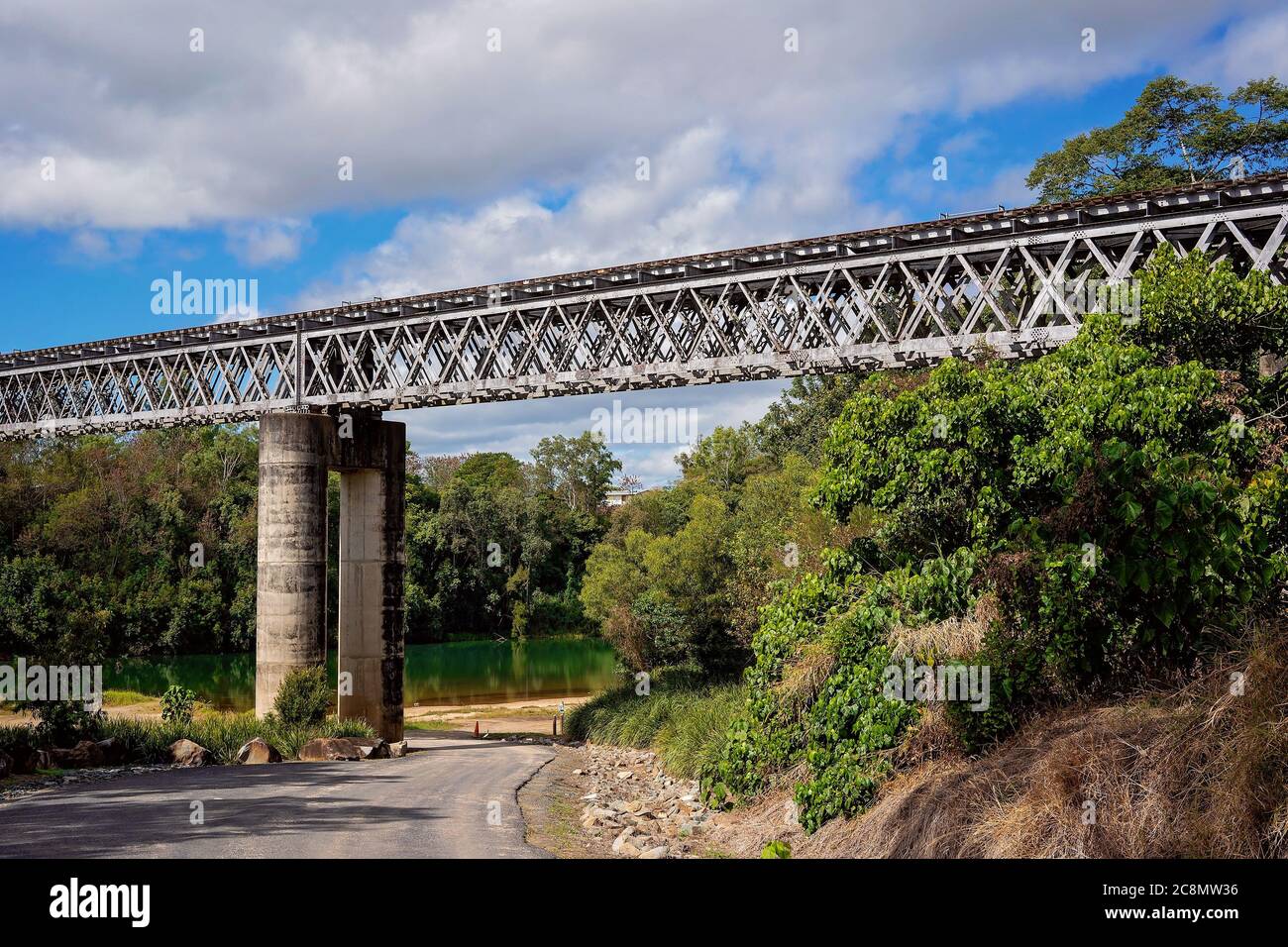 Eine Eisenbahnbrücke aus Beton und Stahl über einem Landfluss gegen einen wolkigen blauen Himmel Stockfoto