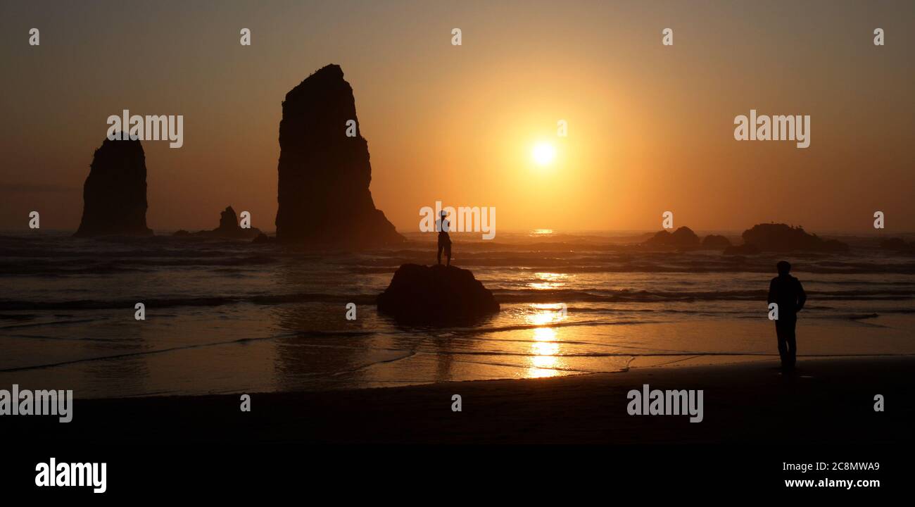 Zwei Männer aus verschiedenen Kulturen blicken einander bei Sonnenuntergang an einer felsigen Küste an. Stockfoto