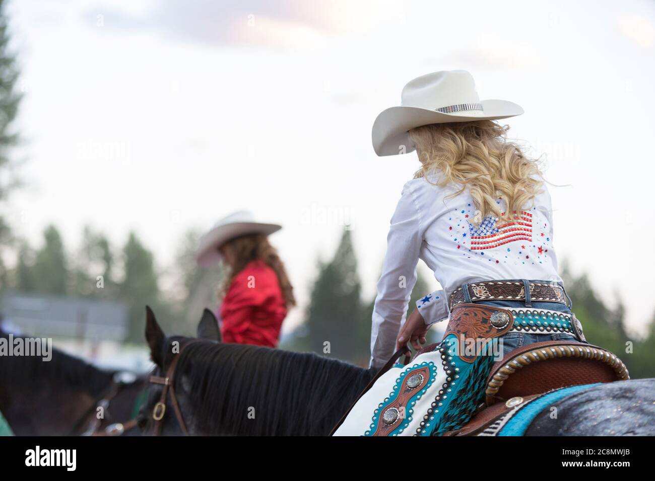 Miss Last Chance Rodeo Queen Cassie Turner (rechts) und Darby Rodeo Queen Abby Riska beugen sich am Freitag, den 24. Juli 2020, während sie einen Moment der Stille in der Kootenai River Stampede in Libby, Montana, erleben. Das jährliche Rodeo wurde mit zusätzlichen Sicherheitsmaßnahmen aufgrund steigender COVID-19-Fälle im Bundesstaat abgehalten. Stockfoto