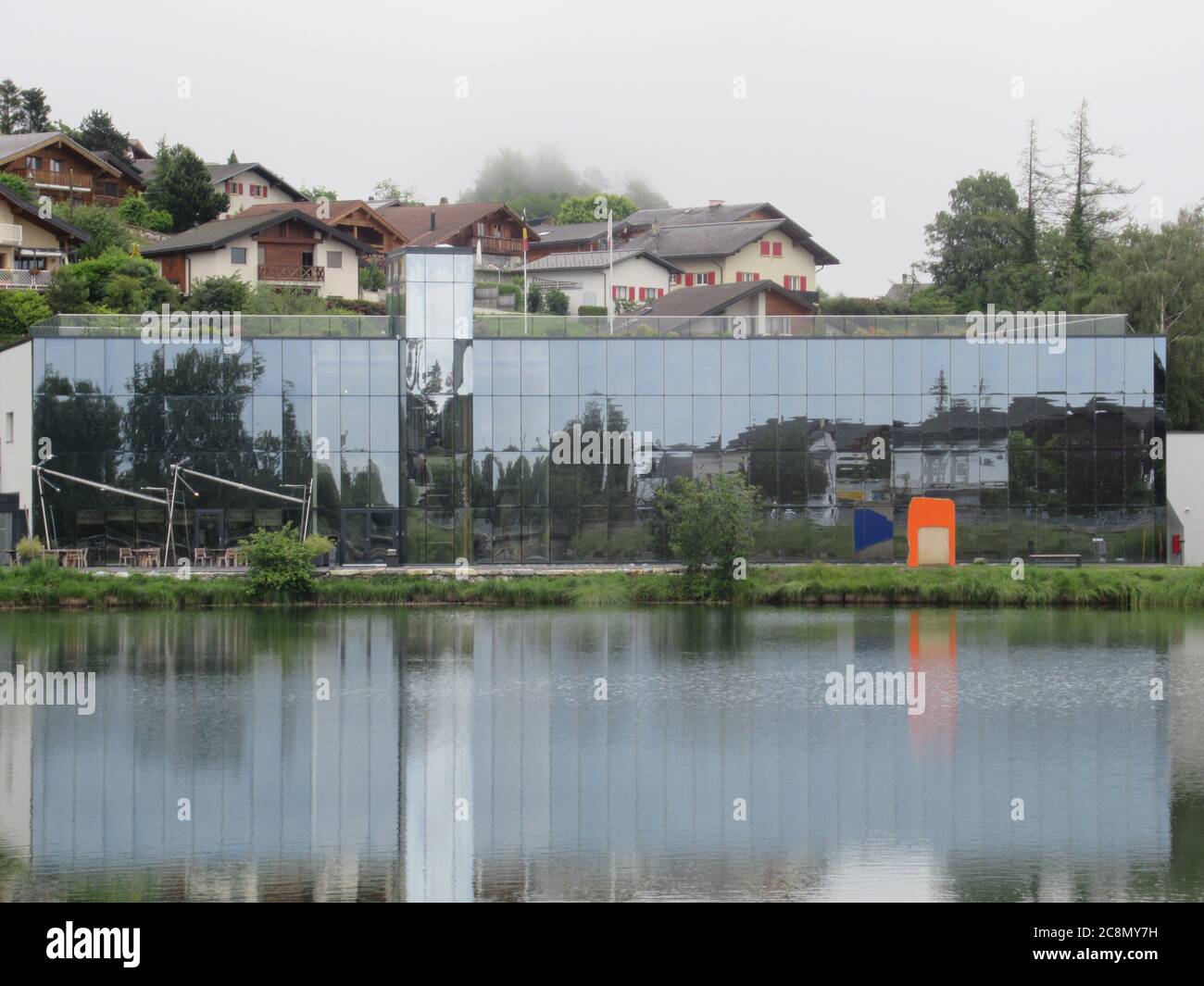 Lens, Schweiz. Juni 2020. Die Fondation Opale, ein Museum für  Aborigine-Kunst. Die façade mit rund 19,000 Photovoltaikmodulen bildet  einen riesigen Spiegel, der die Gipfel des Wallis und den Louche-See  widerspiegelt, an dessen
