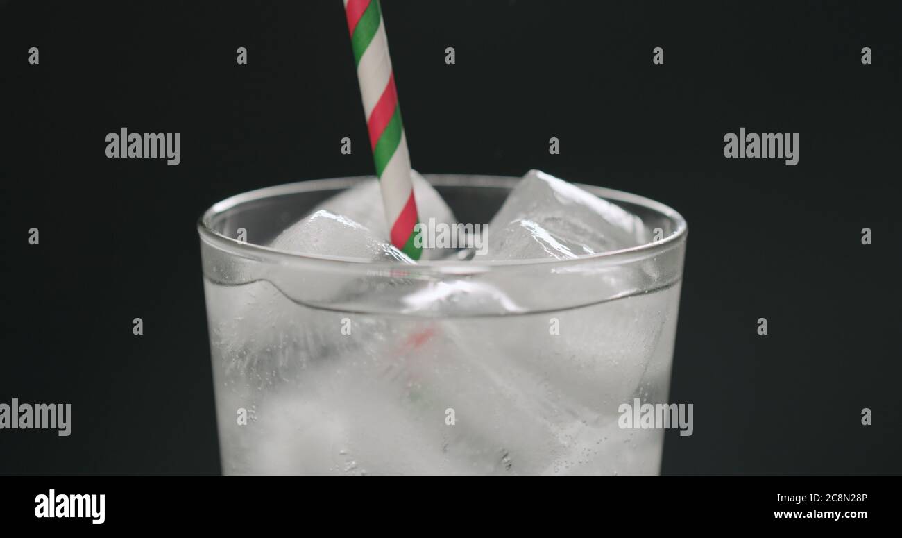Trinken Sie mit Papier Stroh Soda aus Glas mit Eiswürfeln Auf schwarzem Hintergrund Nahaufnahme Stockfoto