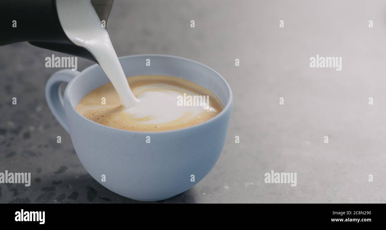 Gieße gedämpfte Milch in Espresso, um Cappuccino in Blau zuzubereiten becher auf betonem Hintergrund Stockfoto