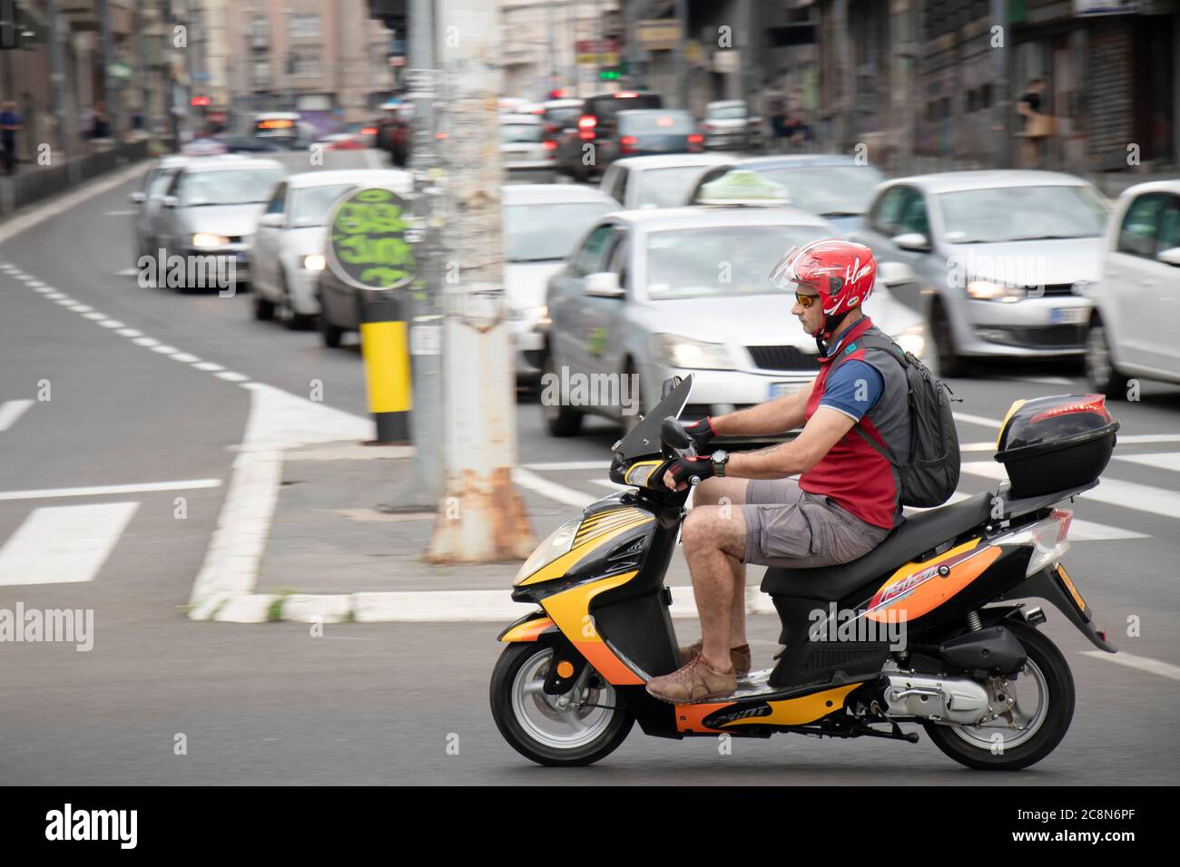 Belgrad, Serbien - 16. Juli 2020: Reifer Mann auf einem Motorroller im Stadtverkehr, auf der Kreuzung mit Autos in der Schlange Stockfoto