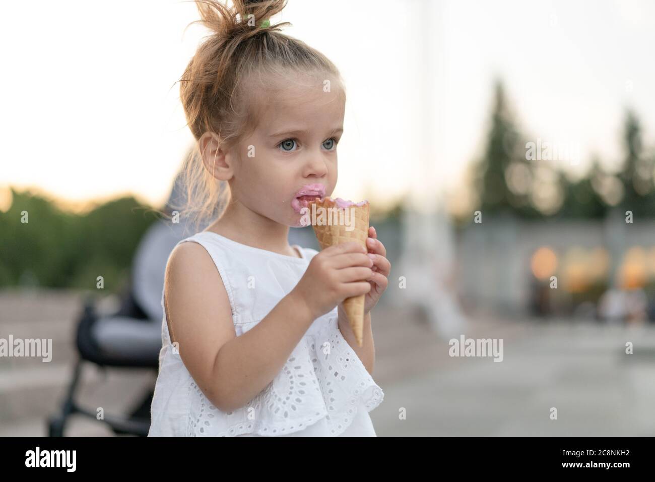 Kleine kaukasische Mädchen 3 Jahre alt isst Eis Nahaufnahme Porträt. Sommerzeit. Kind mit gefrorenem Dessert in der Hand zu Fuß im Freien. Nahaufnahme Porträt europäische Mädchen mit Eis. Stockfoto
