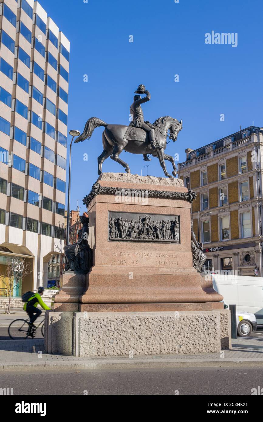 Statue des Prinzen Albert, der seinen Hut (Holborn Circus) gegen den blauen Himmel hebt, mit Inschrift und Tafel, die auf dem roten Granitsockel deutlich sichtbar ist. Stockfoto