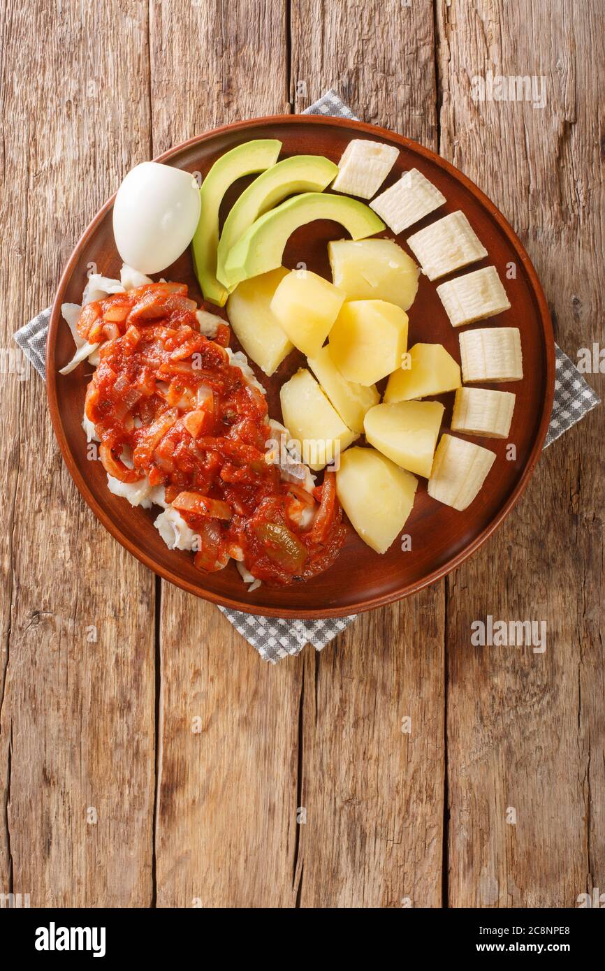 Bermuda traditionelles Frühstück mit gesalzenem Kabeljau mit Zwiebeltomate-Sauce, gekochten Kartoffeln, Eiern, Banane und Avocado in Nahaufnahme auf einem Teller auf dem Tisch. Verti Stockfoto