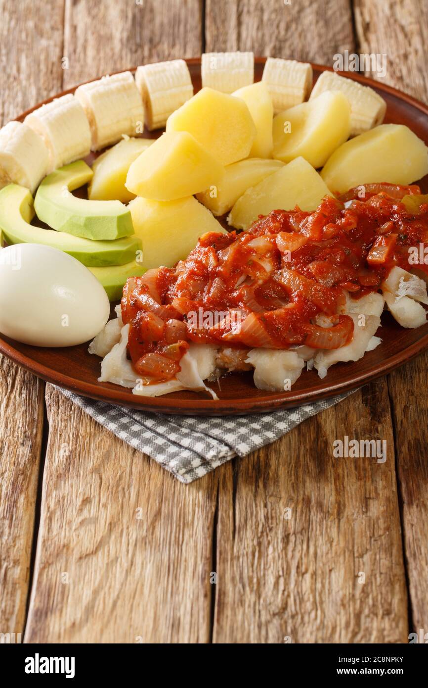 Bermuda traditionelles Frühstück mit gesalzenem Kabeljau mit Zwiebeltomate-Sauce, gekochten Kartoffeln, Eiern, Banane und Avocado in Nahaufnahme auf einem Teller auf dem Tisch. verti Stockfoto