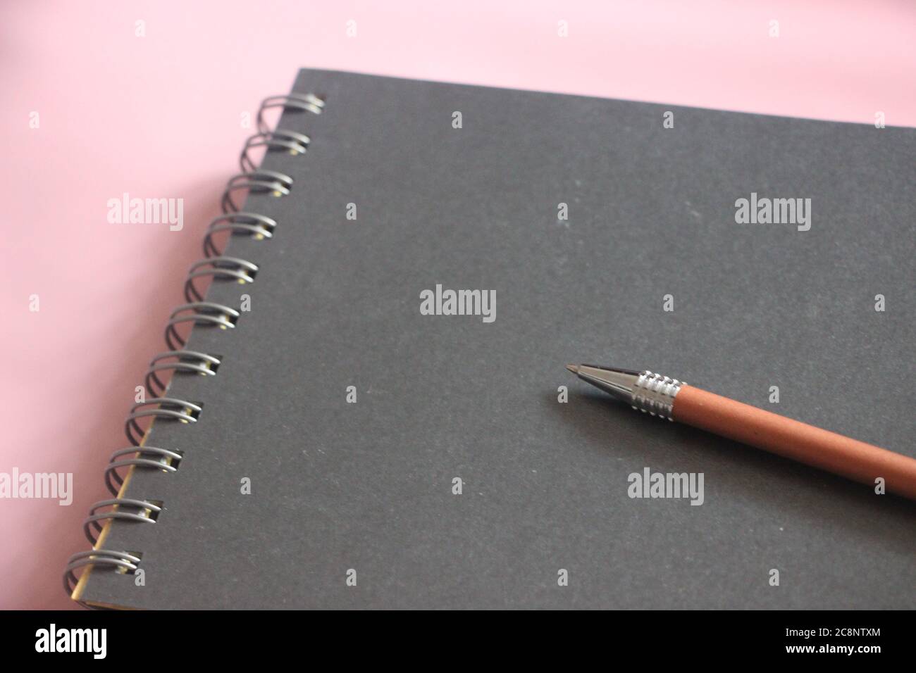 Schwarzer Notizblock mit Stift auf rosafarbenem Tisch. Design-Vorlage mit Copyspace Stockfoto