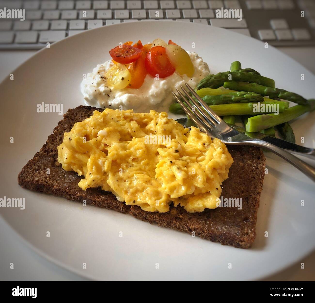 Rührei auf Roggenbrot mit Spargel, Quark und Tomate neben einer Computertastatur Stockfoto