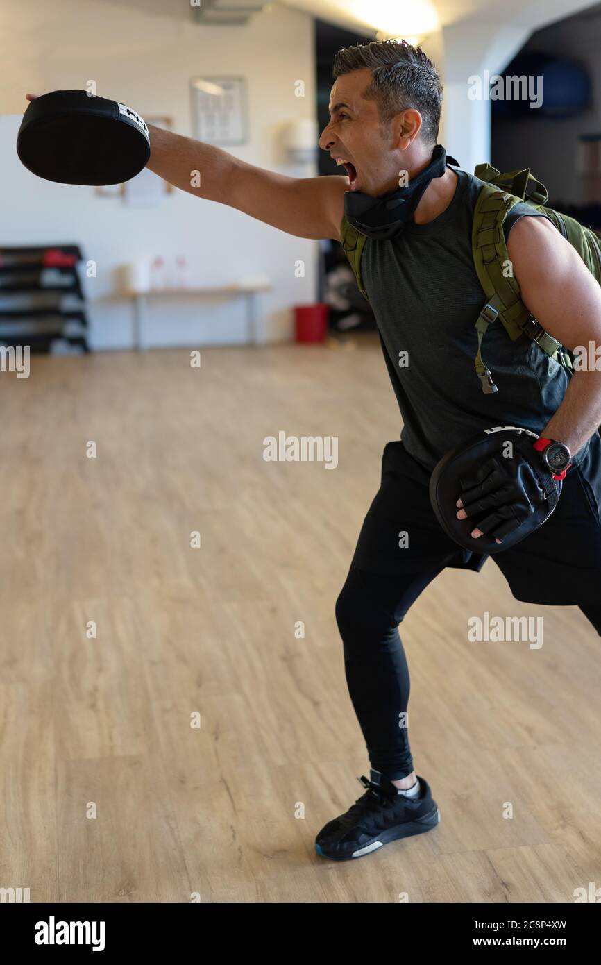 Motivierter Boot Camp Trainer steht mit Schlagschuhen in der Turnhalle. Training mit verlängertem Arm auf Holzboden. Portrait für Fitness-Konzept. Stockfoto
