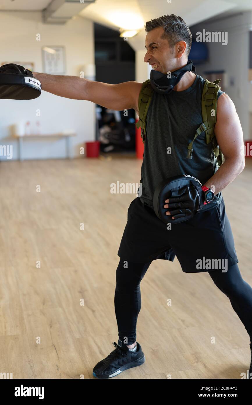 Motivierter Boot Camp Trainer steht mit Schlagschuhen in der Turnhalle. Training mit verlängertem Arm auf Holzboden. Portrait für Fitness-Konzept. Stockfoto
