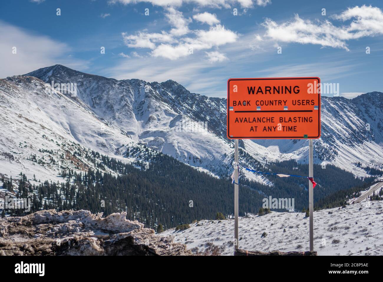 Helles rot/orange Schild mit der Aufschrift Warnung Lawinen Strahlen in bergigen Bereich mit schneebedeckten Bergen im Hintergrund Stockfoto