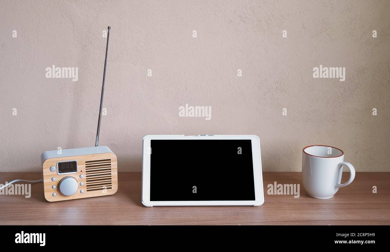 Tablet-Computer mit Retro-Radio und Kaffeetasse auf dem Schreibtisch - leerer Bildschirm und Wand mit Kopierplatz Stockfoto