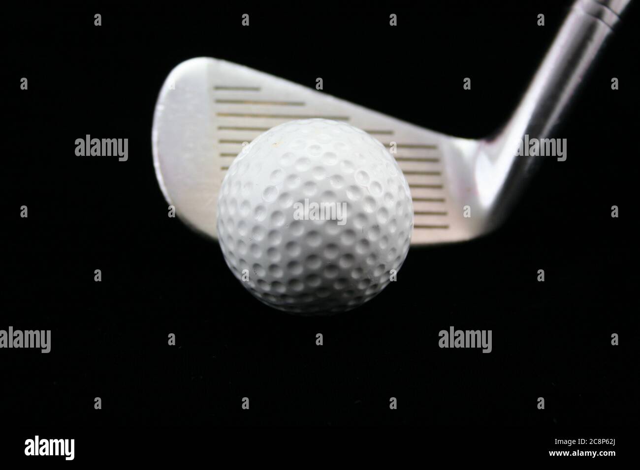 Bild von Golfball mit Golfschlägerkeil auf schwarzem Hintergrund. Stockfoto