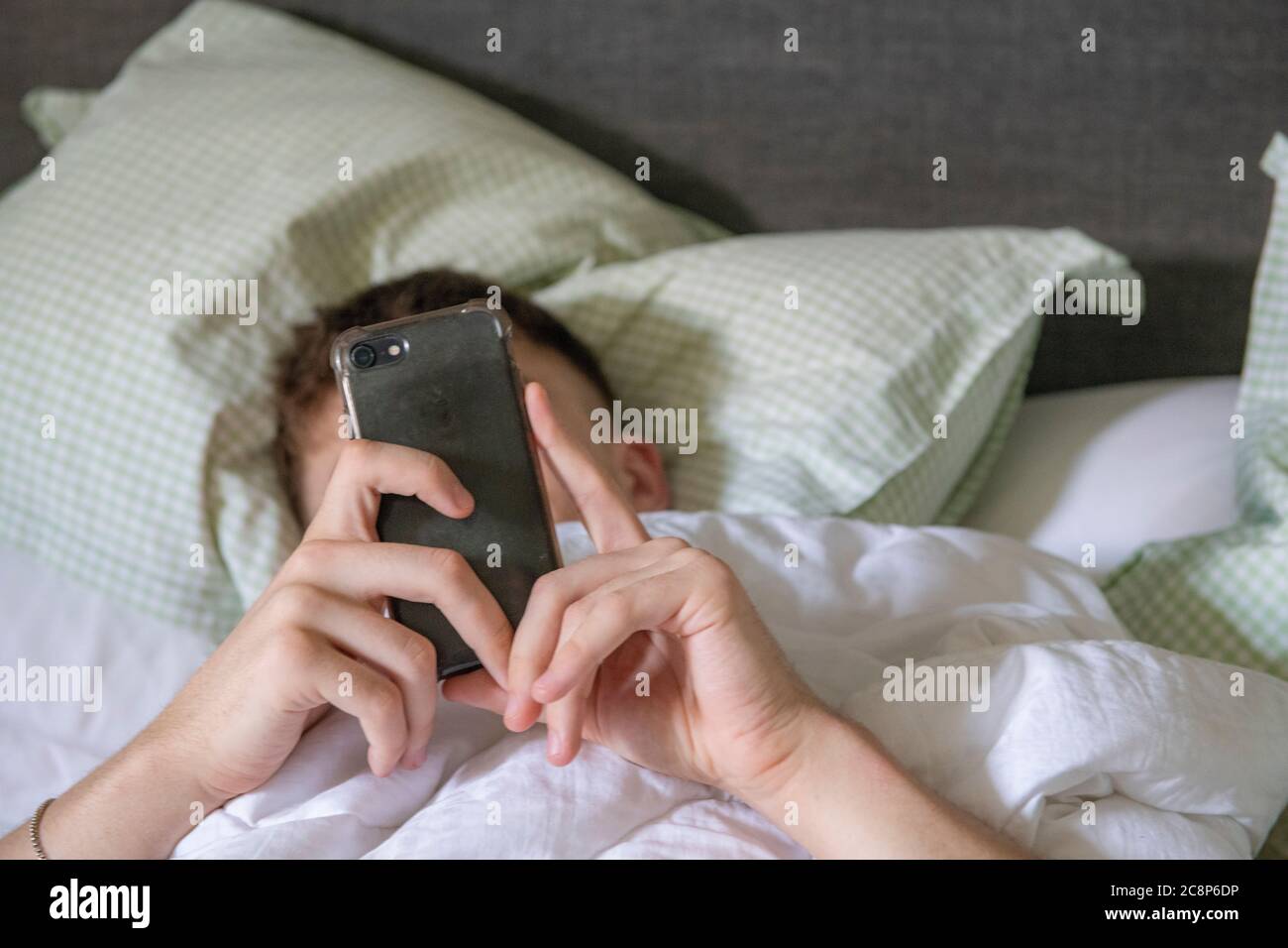 Ein Teenager Junge liegt im Bett mit seinem Handy Stockfoto