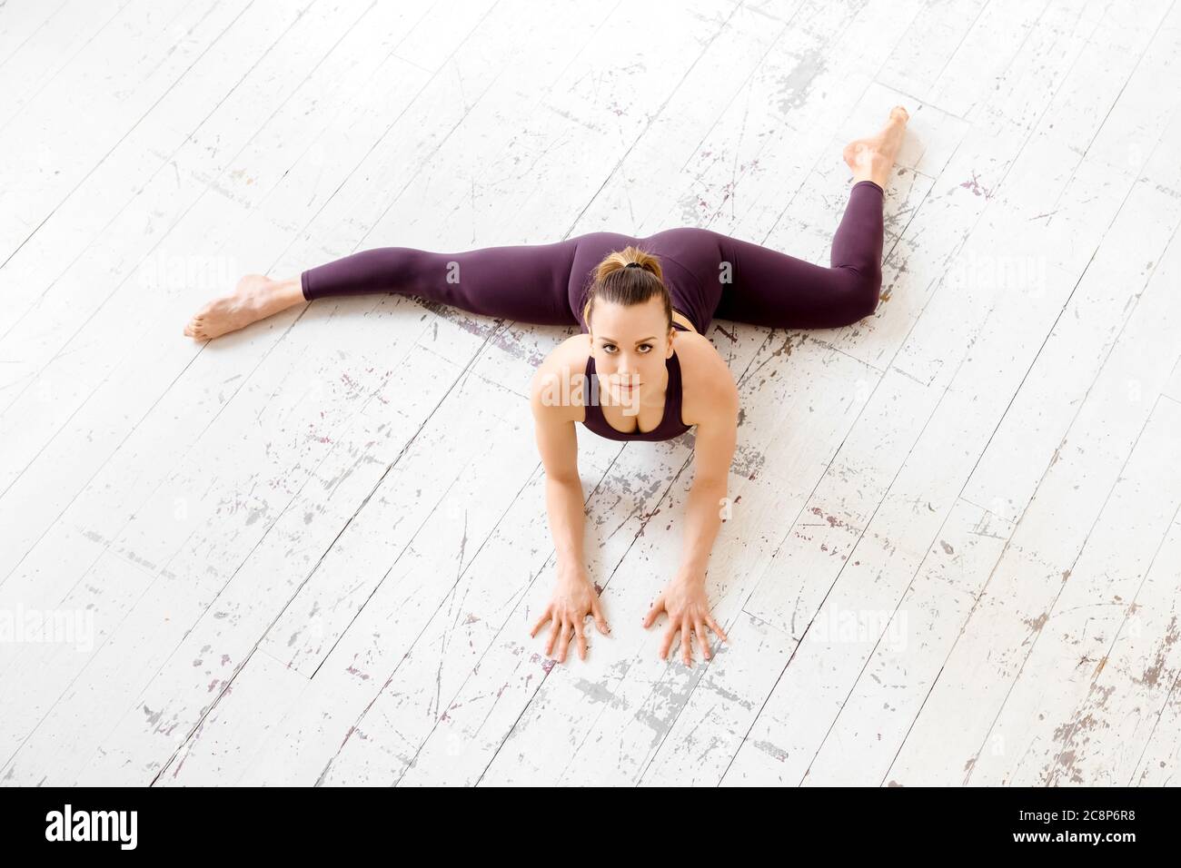 High-Angle-Ansicht einer athletischen jungen Frau, die eine halb frontale geteilte Yoga-Pose auf einem weißen Fitnessboden mit Copyspace in einem Fitness- und aktiven Lebensstil macht Stockfoto
