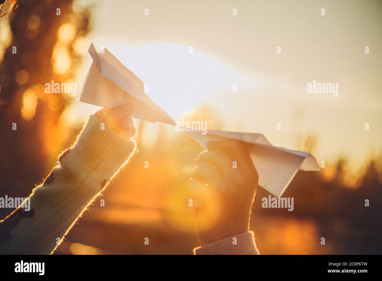 Zwei Papierflugzeuge in Händen, die sich bei Sonnenuntergang anguten. Junge Menschen halten Papierflugzeuge, Liebe, Beziehungen Konzept Stockfoto
