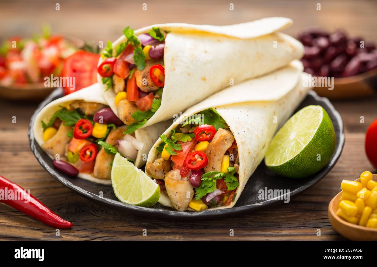 Frische Tortilla Wraps mit Hühnerfleisch und Gemüse auf dem Holztisch Stockfoto