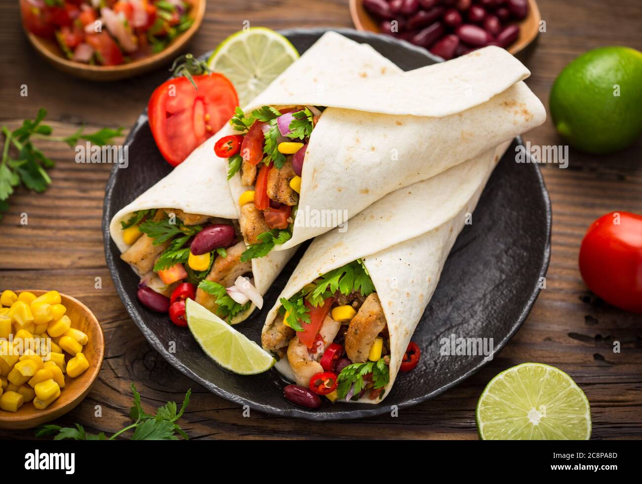 Frische Tortilla Wraps mit Hühnerfleisch und Gemüse auf dem Holztisch Stockfoto