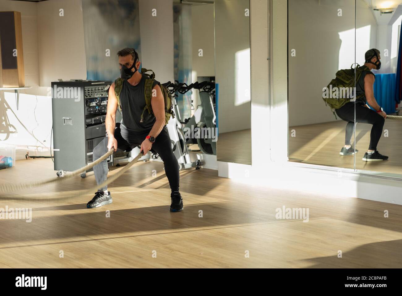 Sportler beim Seiltraining mit Trainingsmaske. Innen auf Eichenboden mit Sonne und Schatten. Für Boot Camp Konzept. Stockfoto