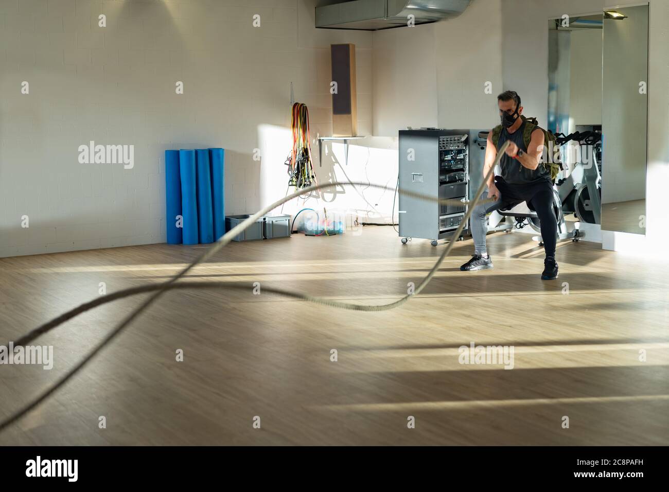 Sportler beim Seiltraining mit Trainingsmaske. Innen auf Eichenboden mit Sonne und Schatten. Für Boot Camp Konzept. Stockfoto