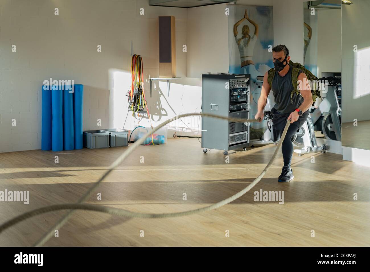 Sportler beim Seiltraining mit Trainingsmaske. Innen auf Eichenboden mit Sonne und Schatten. Für Boot Camp Konzept. Stockfoto