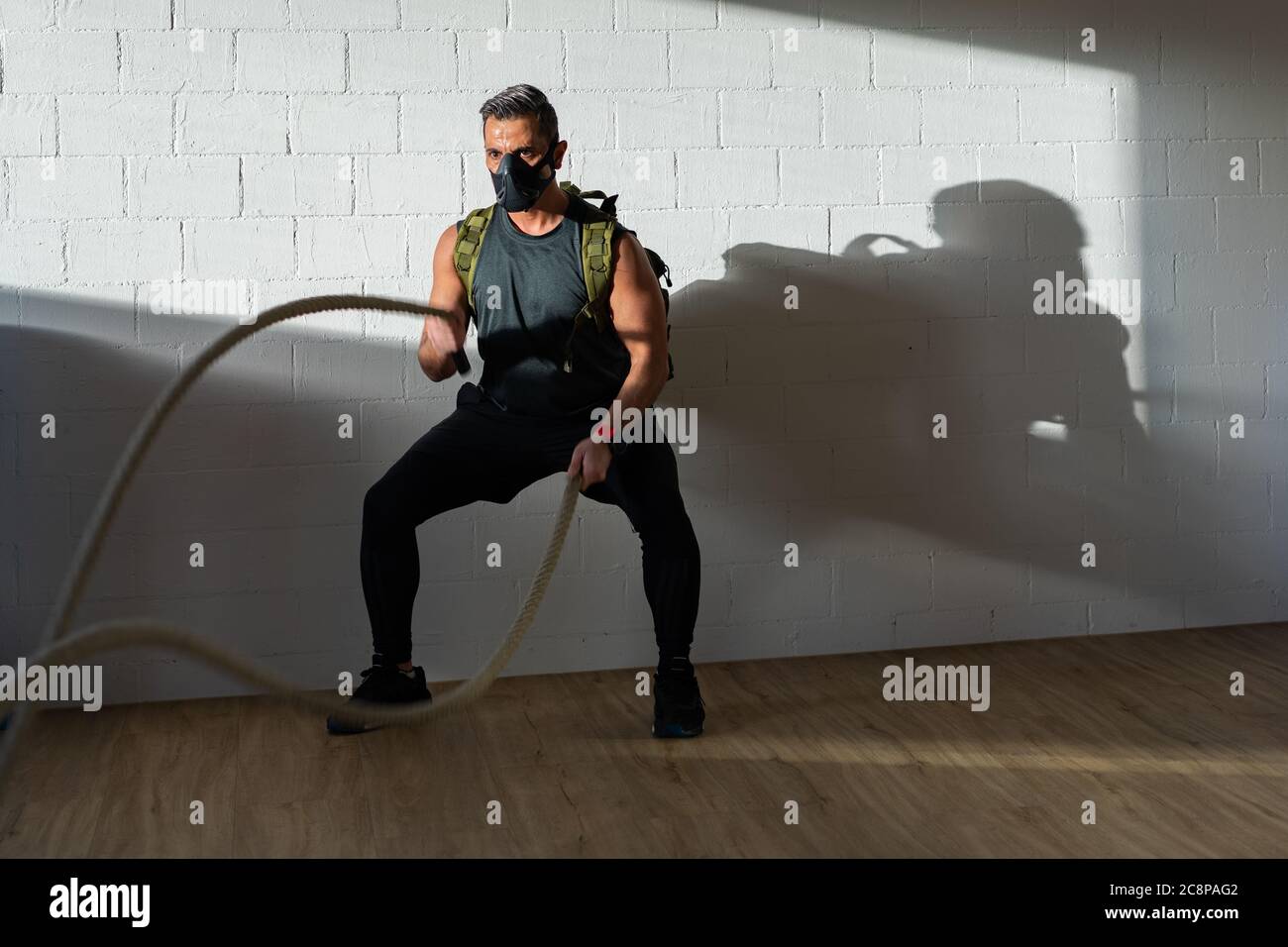 Sportler beim Seiltraining mit Trainingsmaske. Innen auf Eichenboden mit Sonne und Schatten. Für Boot Camp Konzept. Stockfoto