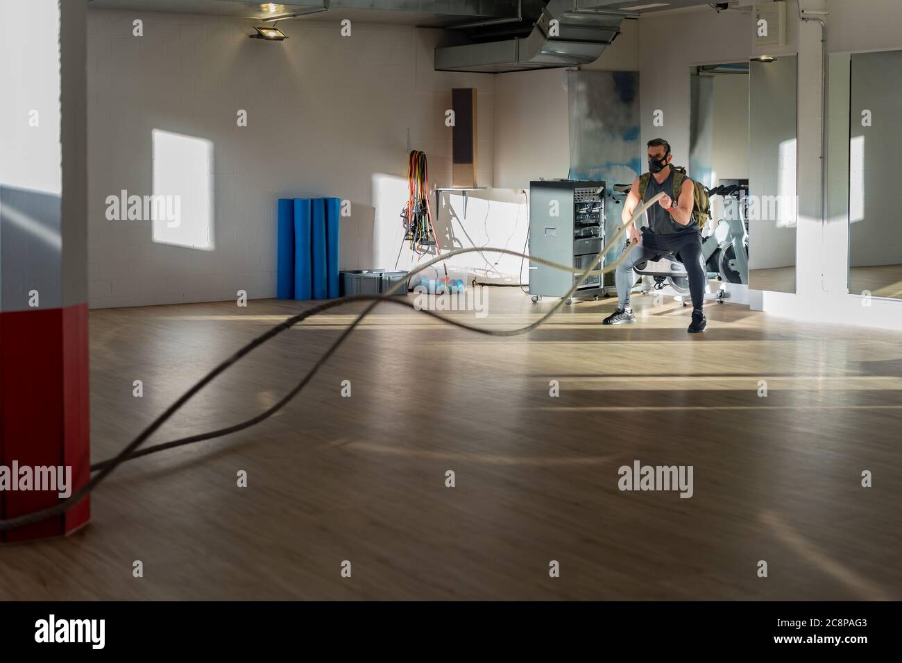 Sportler beim Seiltraining mit Trainingsmaske. Innen auf Eichenboden mit Sonne und Schatten. Für Boot Camp Konzept. Stockfoto