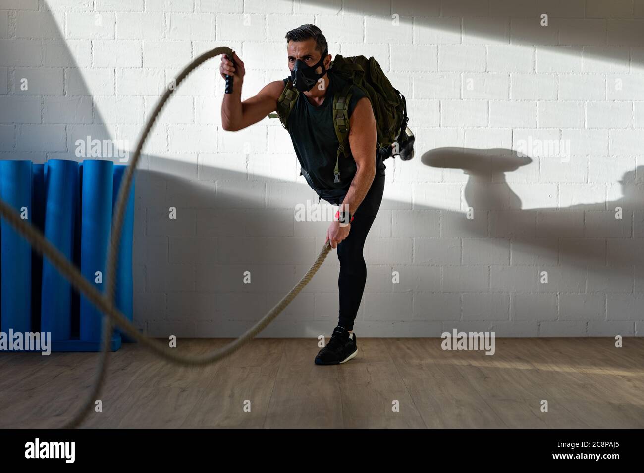 Sportler beim Seiltraining mit Trainingsmaske. Innen auf Eichenboden mit Sonne und Schatten. Für Boot Camp Konzept. Stockfoto