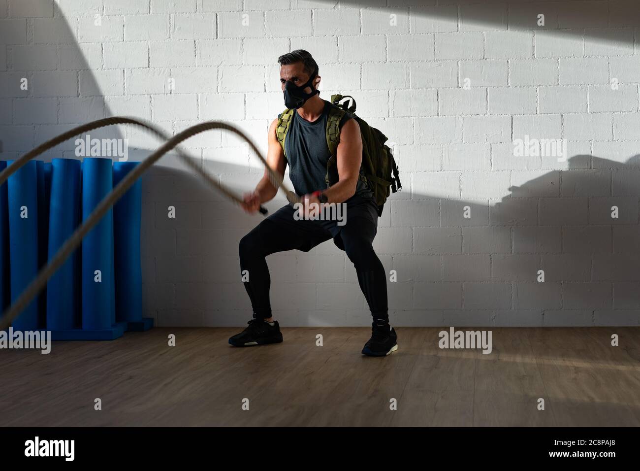 Sportler beim Seiltraining mit Trainingsmaske. Innen auf Eichenboden mit Sonne und Schatten. Für Boot Camp Konzept. Stockfoto
