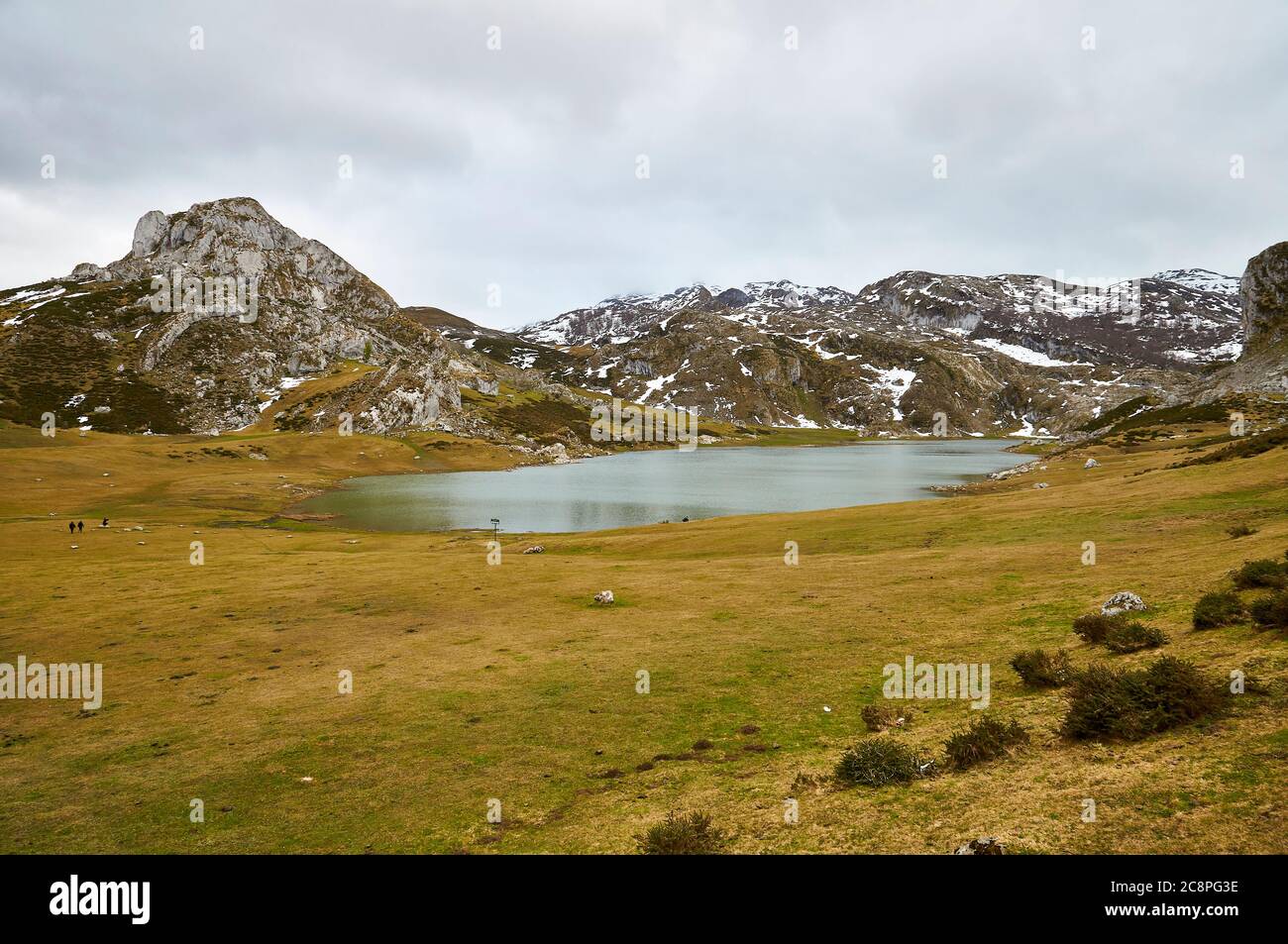 Wanderer rund um den Lago Ercina Gletschersee bei bewölktem Tag mit Schnee in den nahe gelegenen Gipfeln (Cangas de Onís, Nationalpark Picos de Europa, Asturien, Spanien) Stockfoto