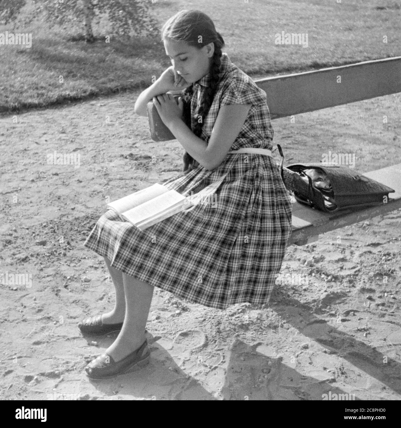 Junge Schülerin mit Zöpfen tragen Kleid sitzen auf Parkbank Schule Lehrbuch 1950er Jahre budapest ungarn Stockfoto