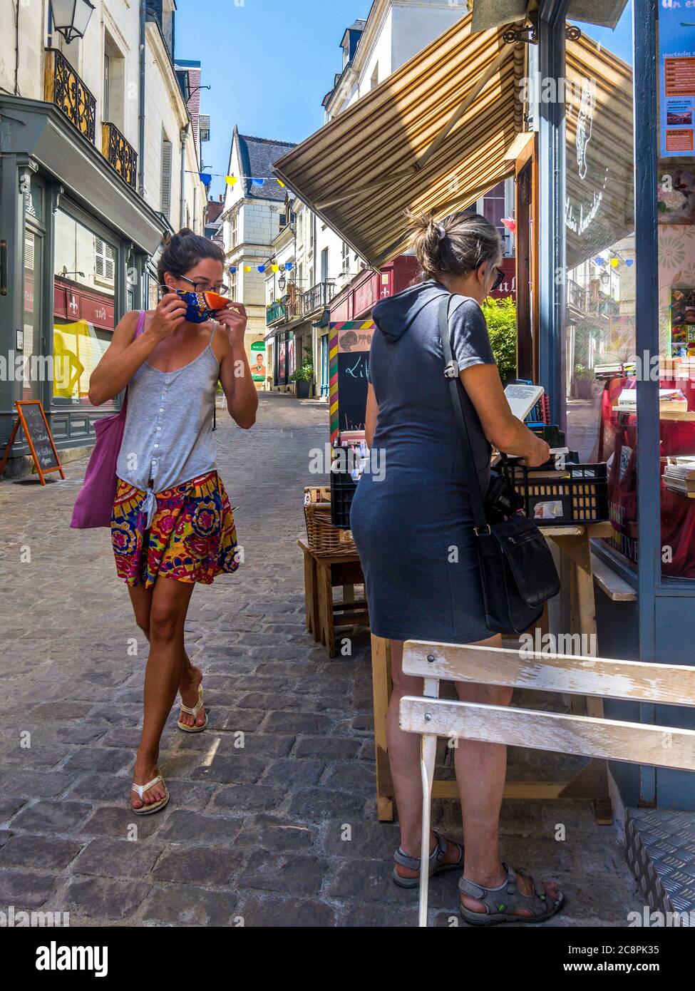 Junge Frau, die Gesichtsmaske aufsetzt, bevor sie in den Laden geht - Loches, Indre-et-Loire, Frankreich. Stockfoto